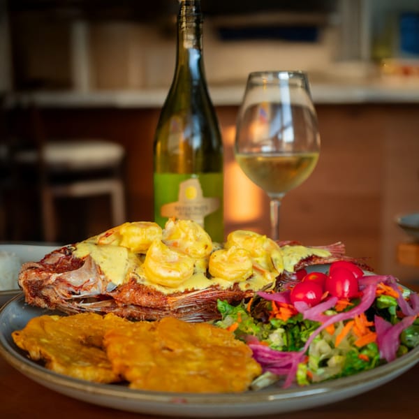 Colombian whole fried fish topped with shrimp in sauce, plantains, and salad with wine.