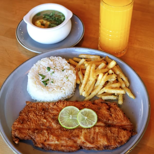 Colombian fried fish with rice, french fries, lime, a side of soup, and orange juice.